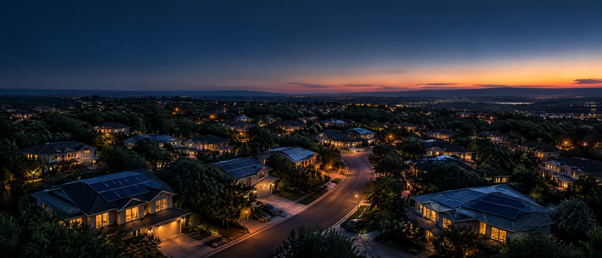 Aerial view of a suburban neighborhood at dusk with solar panels on many rooftops