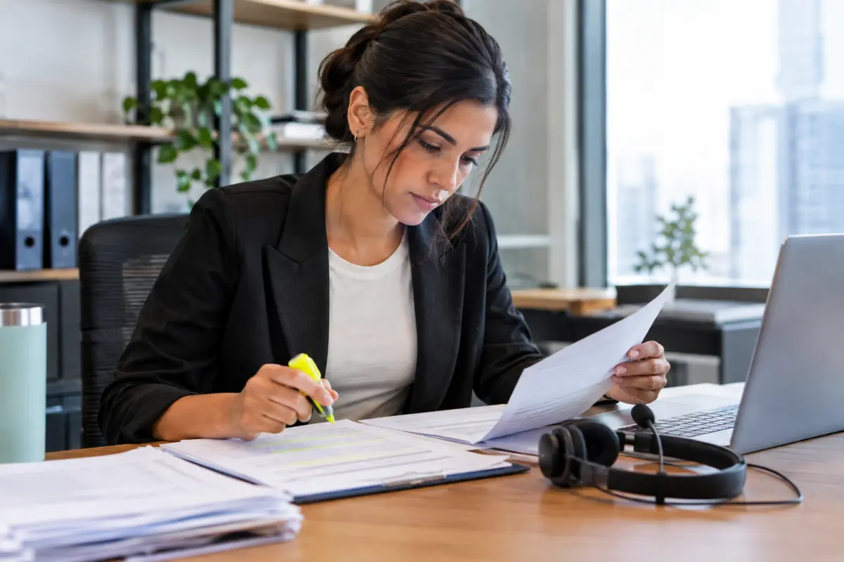 Operations manager reviewing printed call scripts and consent documents at a desk with a headset and laptop