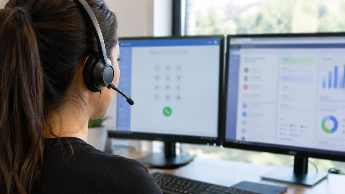Over-the-shoulder view of an appointment setter with a headset working at a dialer and CRM dashboard